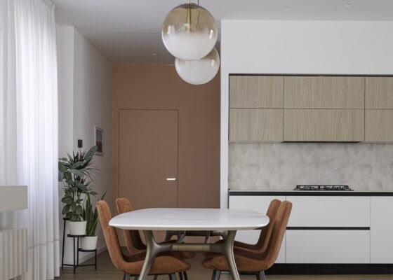 Zona giorno con tavolo da pranzo, cucina lineare bianca e porta filo muro color terracotta in un appartamento in centro a Piove di Sacco (Padova)