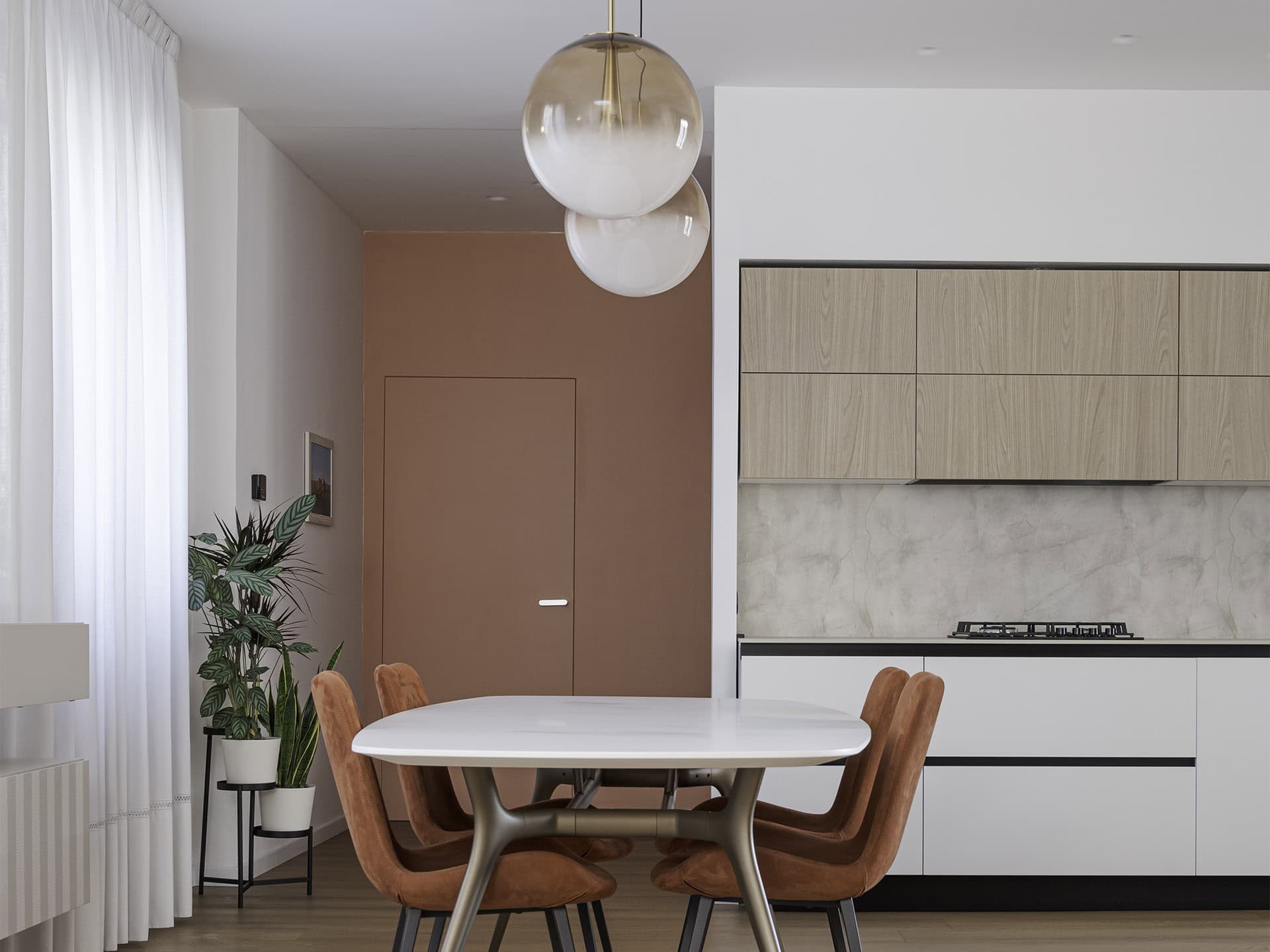 Zona giorno con tavolo da pranzo, cucina lineare bianca e porta filo muro color terracotta in un appartamento in centro a Piove di Sacco (Padova)