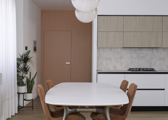 Zona giorno con tavolo da pranzo, cucina lineare bianca e porta filo muro color terracotta in un appartamento in centro a Piove di Sacco (Padova)