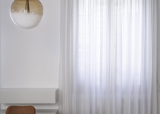 Lampada a sospensione con sfera in vetro e tende bianche filtranti nella zona pranzo